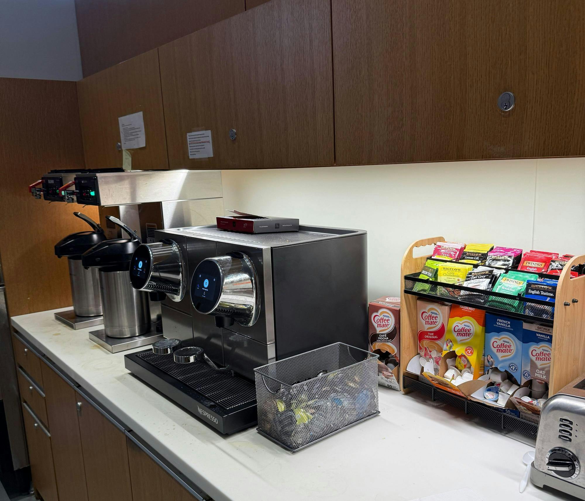 Coffee machines on surface, next to an array of tea bag packets and coffee pods. 
