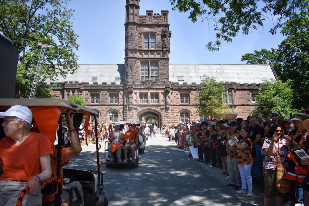 People in bright orange garb lining a path. Some ride golf carts. In the background is a brown building.