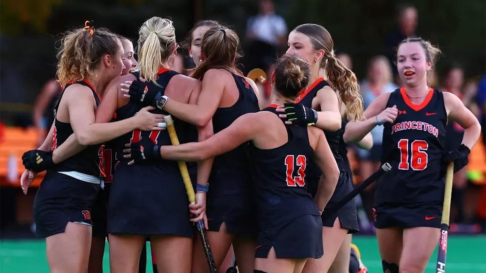 Princeton field hockey team celebrating after a goal; people in black and orange outfits