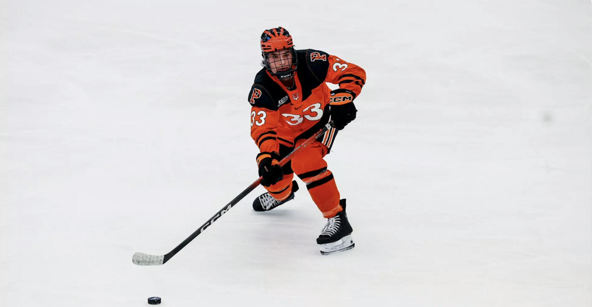 Princeton men's ice hockey player in orange and black passing a puck.