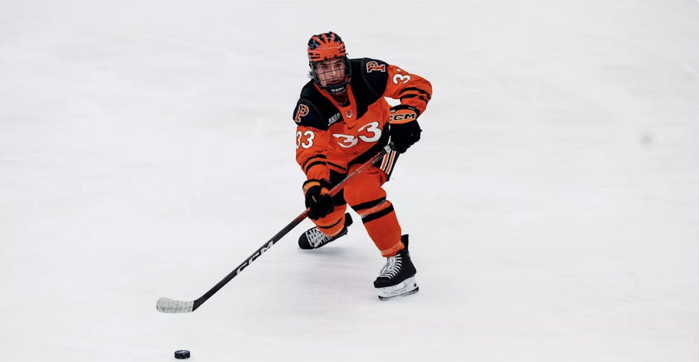 Princeton men's ice hockey player in orange and black passing a puck.