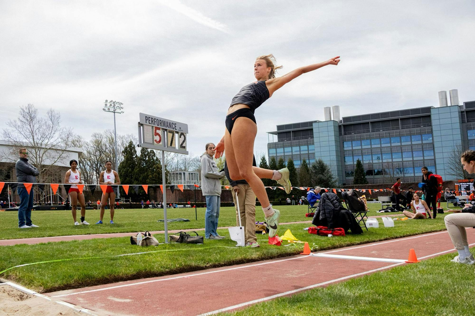 Green grass in background, red jumping lane in foreground with woman flying through air above.