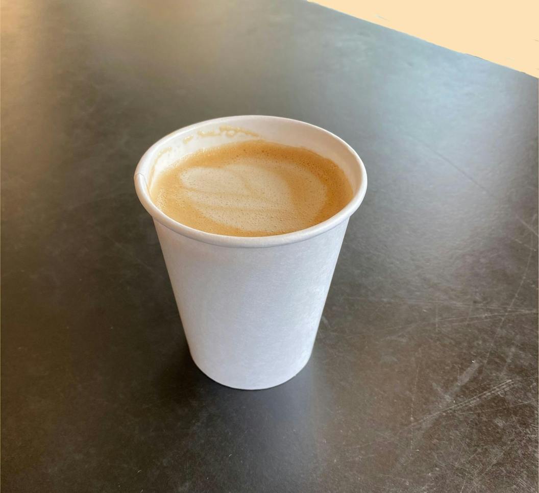A warm flat white sits on a table against a light orange background.