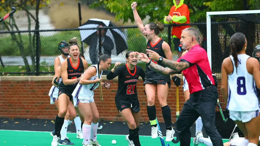 Princeton players in black uniforms cheer and one of the players jumps in the air pumping her fist.