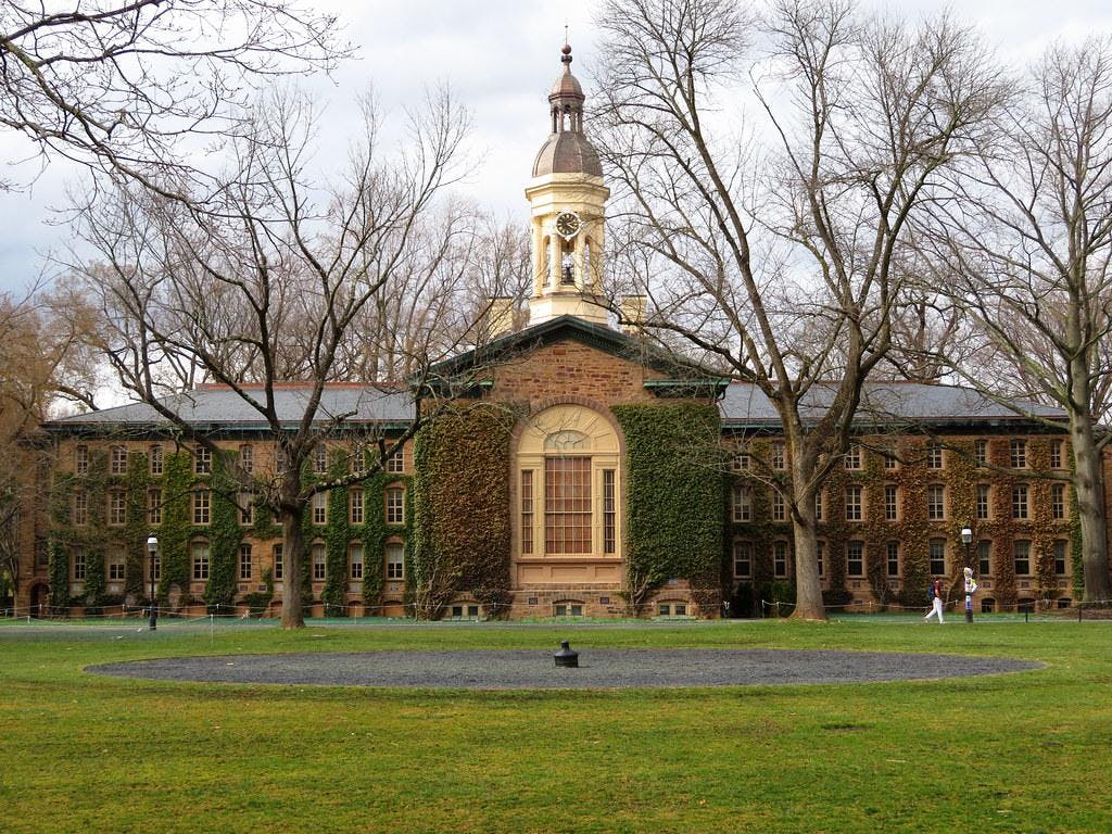 The top of a cannon buried in a green field in front of an ivy-covered building.