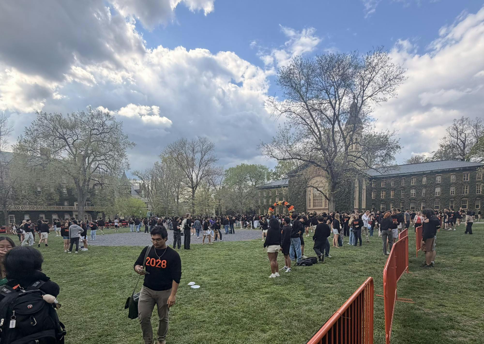 Students in black sweaters gathered on a lawn, with orange gates and balloon displays. 