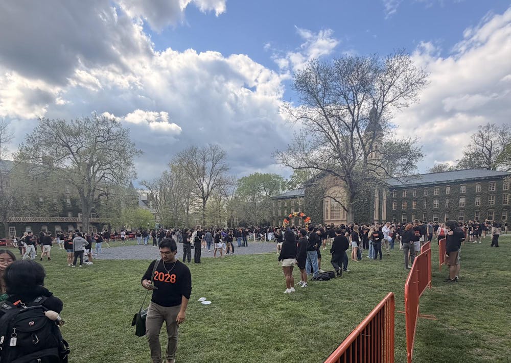 Students in black sweaters gathered on a lawn, with orange gates and balloon displays. 