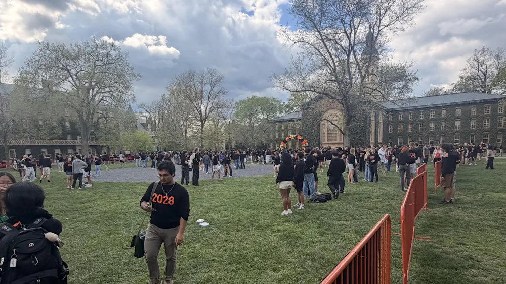 Students in black sweaters gathered on a lawn, with orange gates and balloon displays.