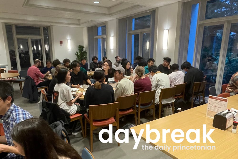 A crowd of people sit around a rectangular table, speaking with each other. In the bottom right, a logo reads “Daybreak: daily princetonian”