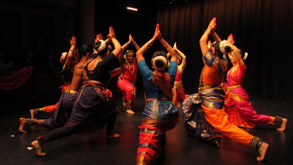 A group of dancers in colorful clothing strike a pose together in a large circle 