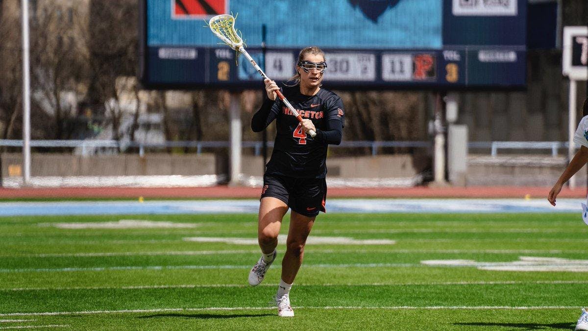 Player in black and orange Princeton uniform runs with lacrosse ball up the field. 