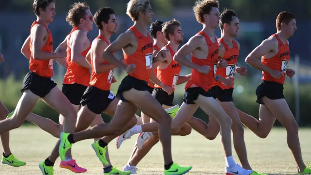 Nine Princeton members of the men's cross country team, dressed in an orange tank top and black shorts, running during warm-ups. 