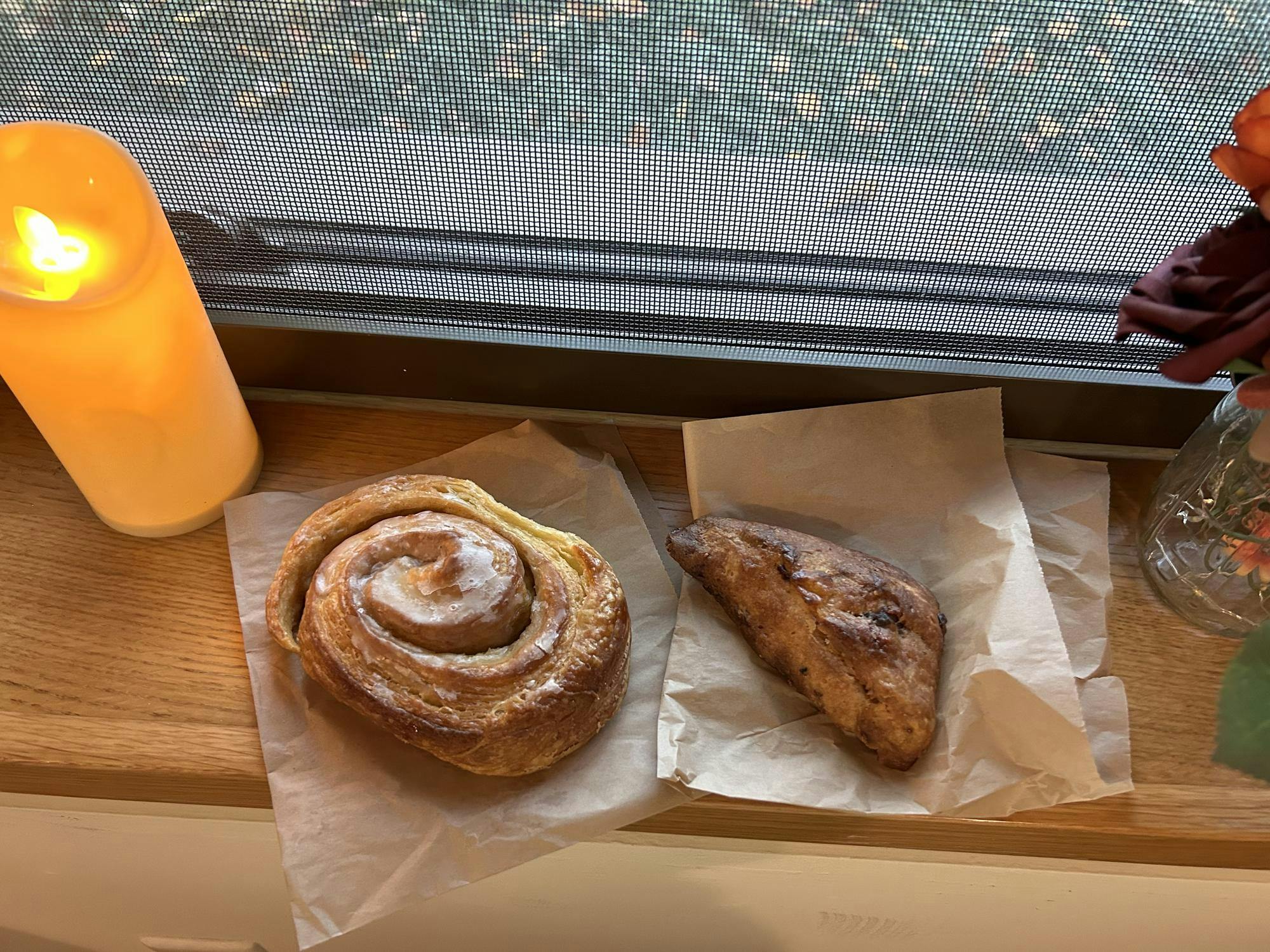 Two pastries sitting on parchment table on a brown table near a candle.