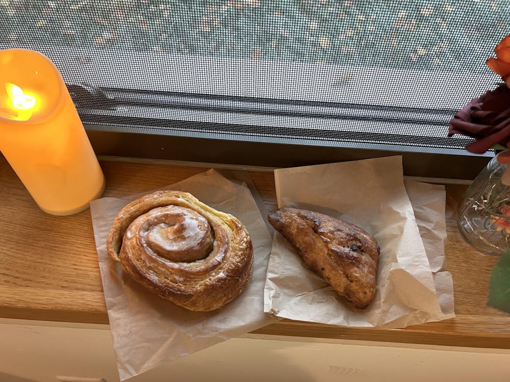 Two pastries sitting on parchment table on a brown table near a candle.