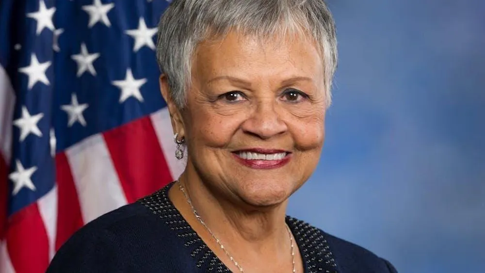 Una foto de la representante estadounidense Bonnie Watson Coleman sonriendo frente a una bandera estadounidense sobre un fondo azul.