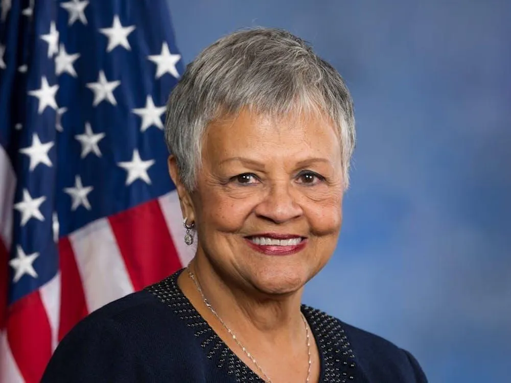 Una foto de la representante estadounidense Bonnie Watson Coleman sonriendo frente a una bandera estadounidense sobre un fondo azul.
