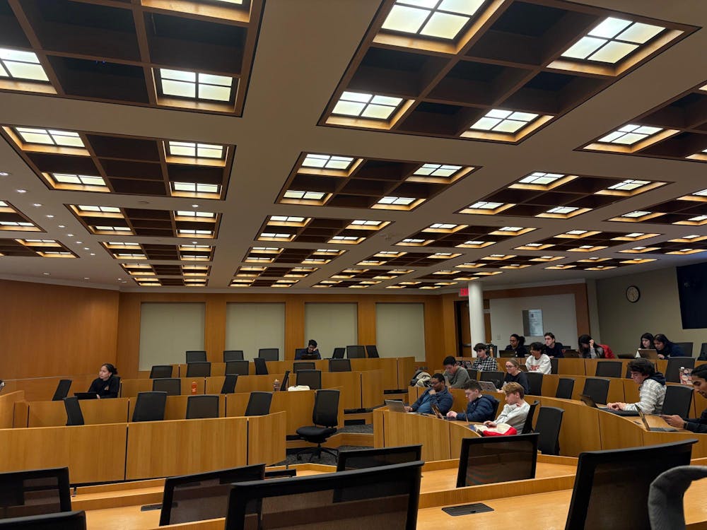 In a wood-paneled room, a small group of students sit at tiered tables.