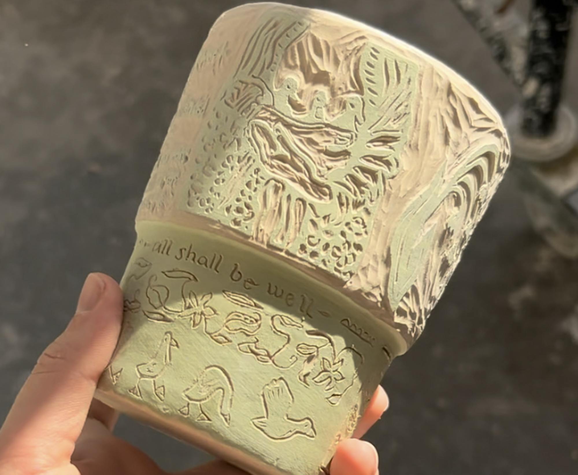 A light green and white pottery vessel with written word and images carved into it.