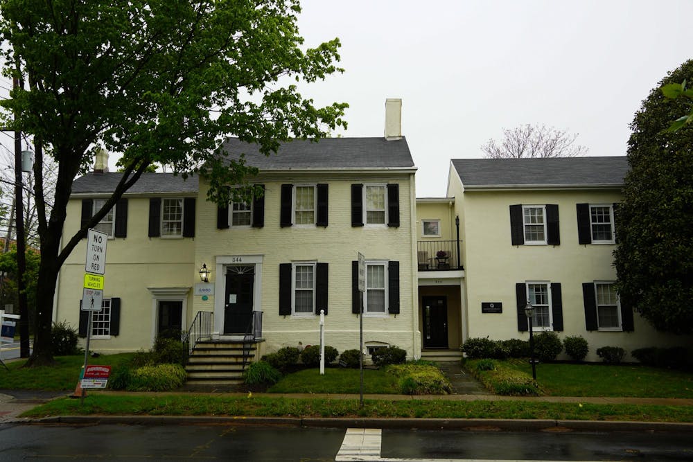 A yellow house with windows with black shutters, with a tree on the left and a hedge on the right of the house.