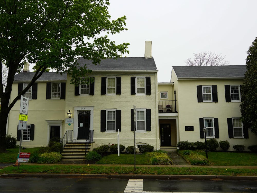 A yellow house with windows with black shutters, with a tree on the left and a hedge on the right of the house.