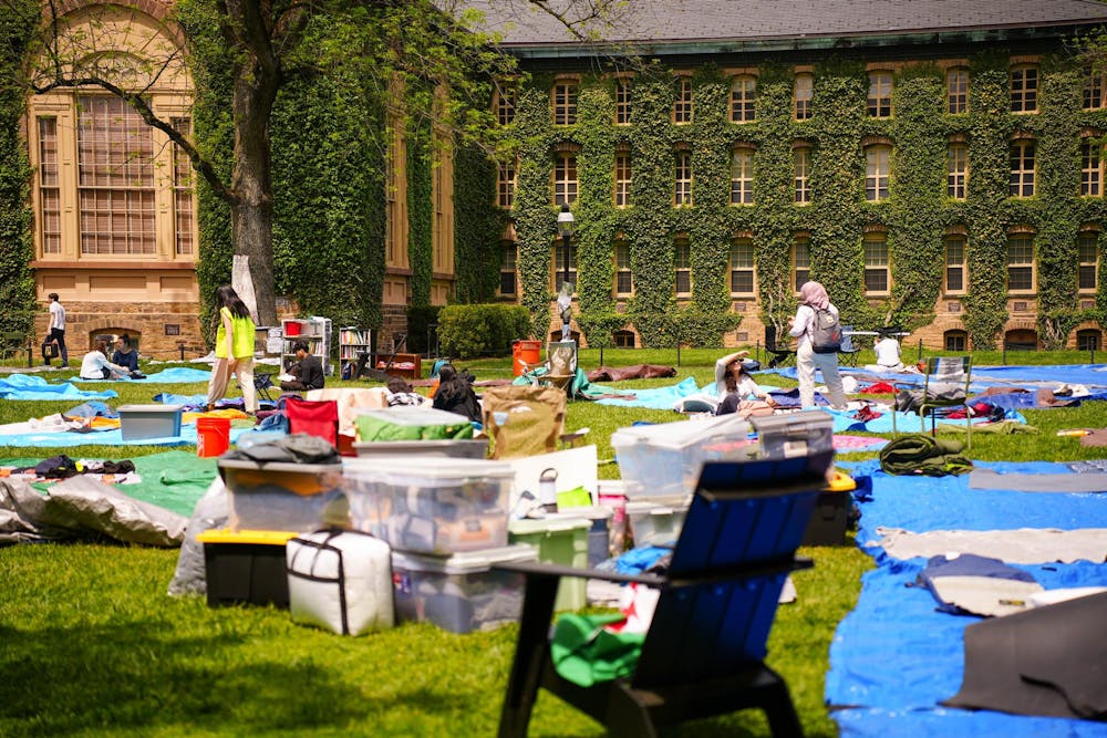 Boxes and tarps piled on a green lawn, with students standing around them. In the background, a stone building covered in ivy.