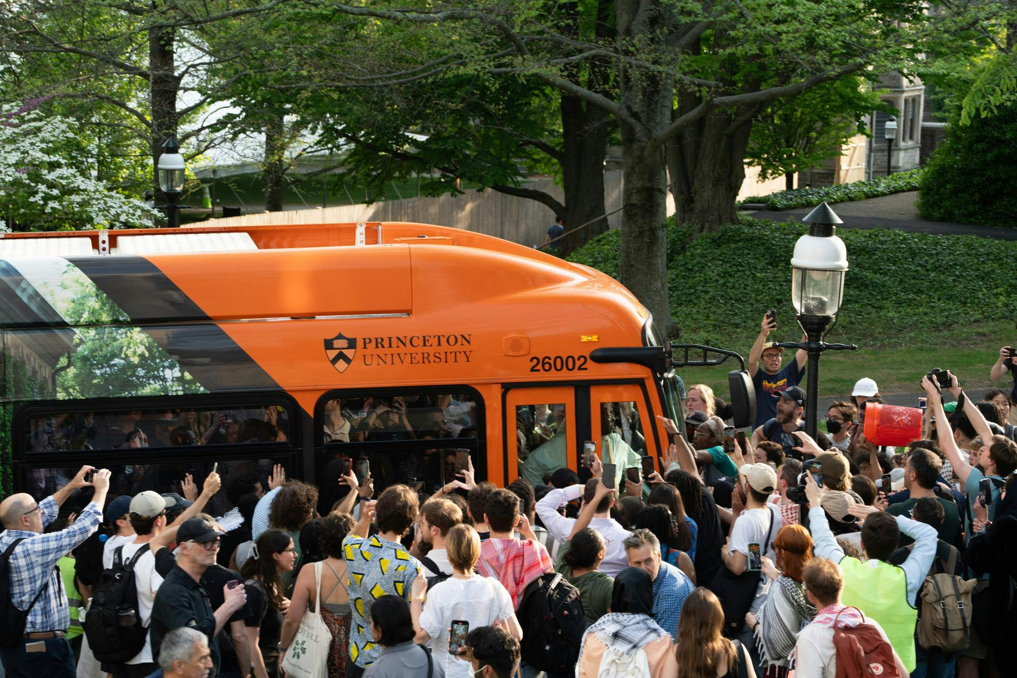 Many people surround a black and orange Princeton bus from the front and side of it.