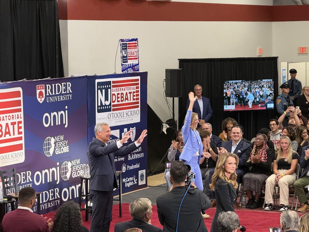 Two people are stood in front of a wall with various logos for newspapers on it. They are waving at a large crowd.