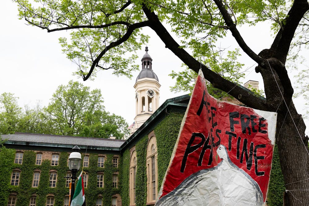 A sign hanging from a tree that reads "FREE FREE PALESTINE" partially covers an ivy covered building in the background.