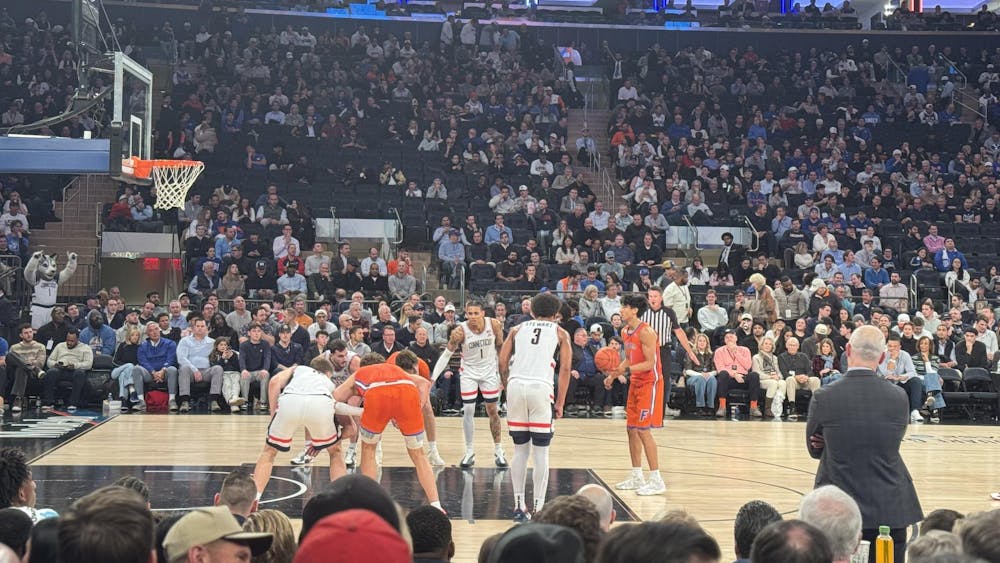 A basketball player prepares to shoot a free throw as players line up along the lane, with a referee and coach on the sideline and a packed arena crowd in the background.