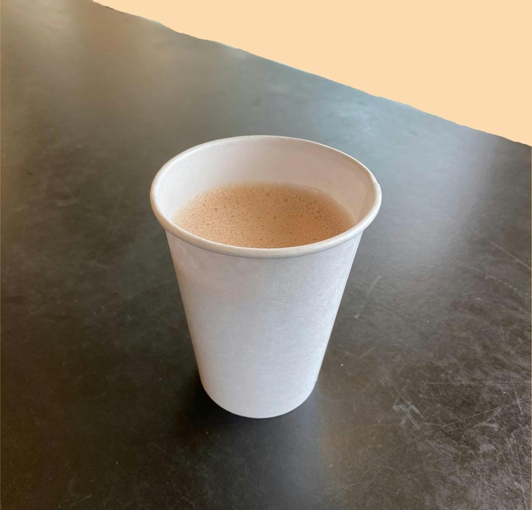 A warm cup of butter pecan chai sits on a table in front of a light orange background.