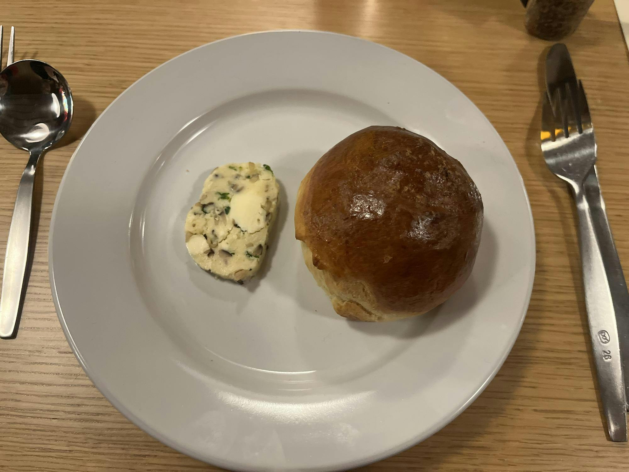 The brown role and a chunky green and white butter sit on a white plate.