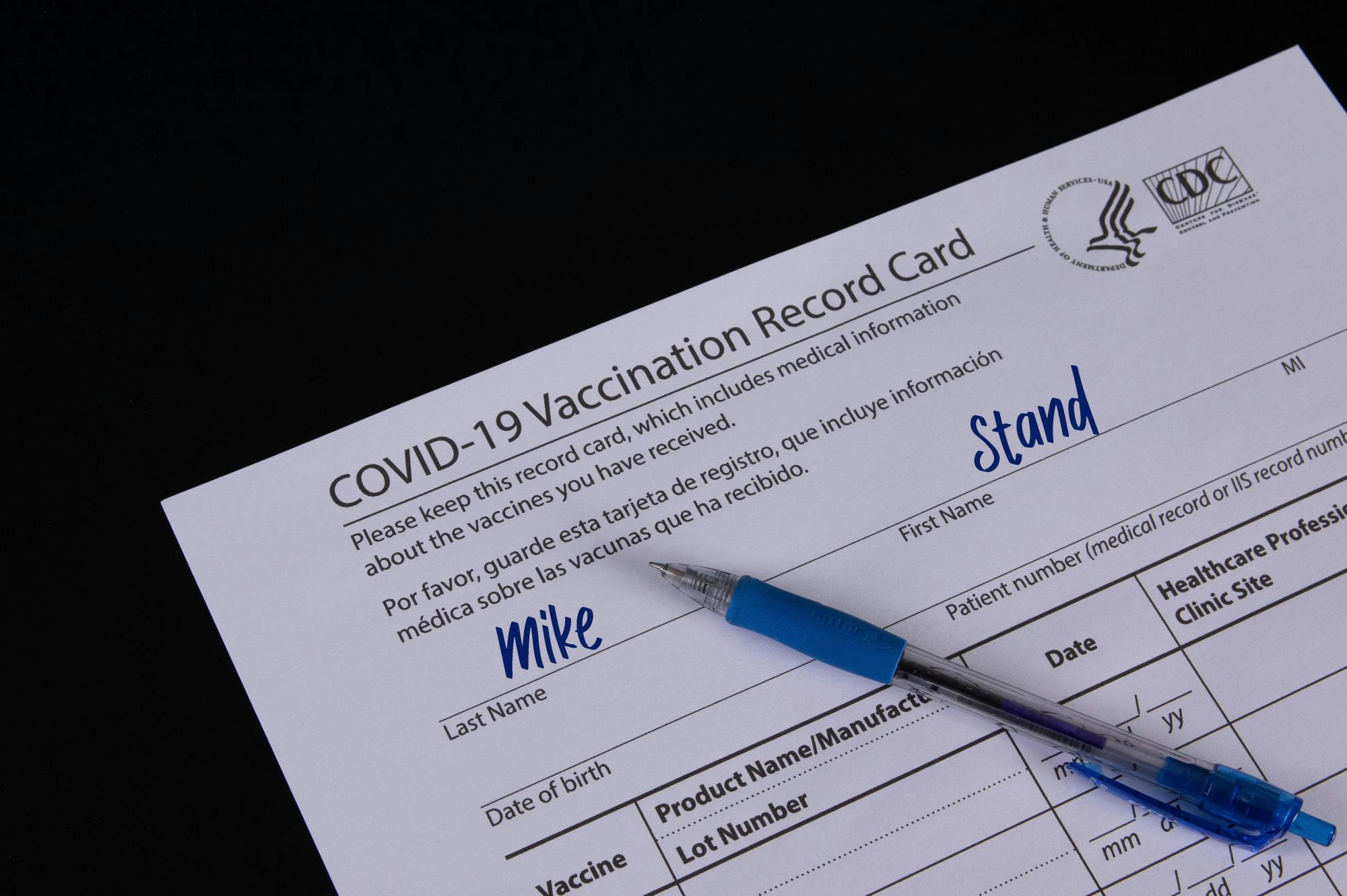 COVID-19 Vaccination record card and a blue pen on black backgro