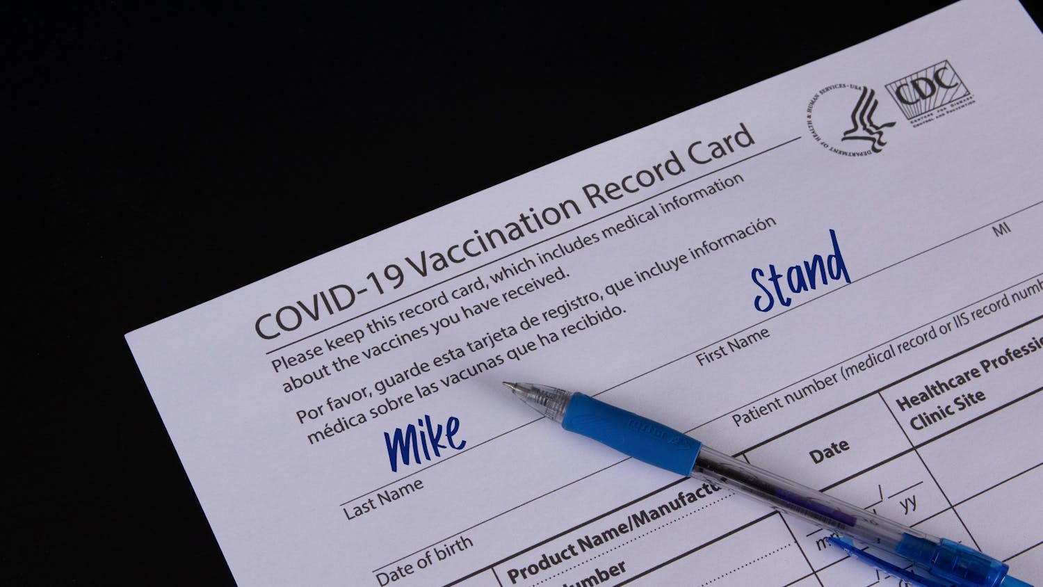 COVID-19 Vaccination record card and a blue pen on black backgro