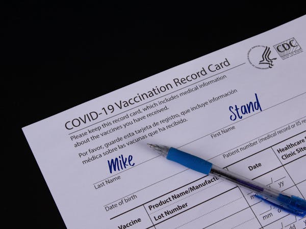 COVID-19 Vaccination record card and a blue pen on black backgro