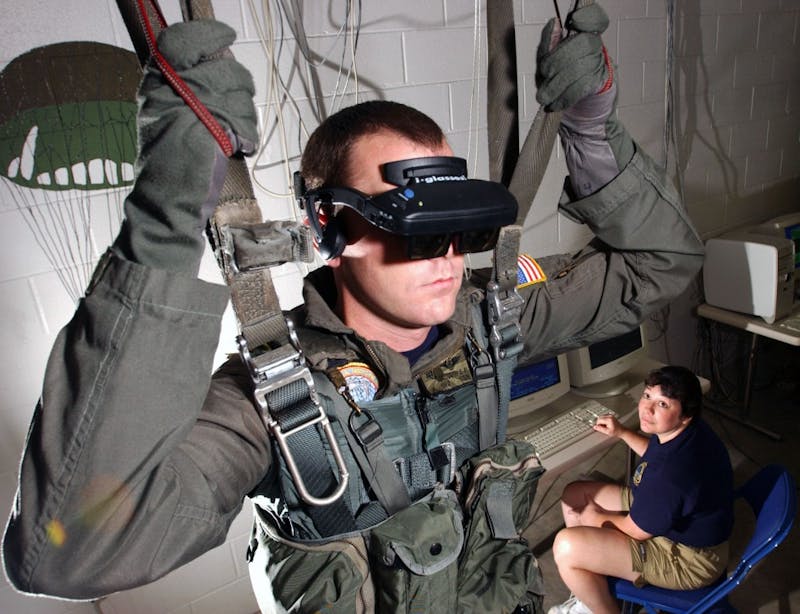 021115-N-5862D-001
Aboard Naval Air Station (NAS) Pensacola (Nov. 15, 2002) -- Hospital Corpsman 2nd Class Tim Sudduth, from Vashowish, Wash., demonstrates the Virtual Reality (VR) parachute trainer, while Aviation Survival Equipmentman 1st Class, Jackie Hilles, from Ekland, Penn., controls the program from a computer console.  Students wear the VR glasses while suspended in a parachute harness, and then learn to control their movements through a series of computer-simulated scenarios. The computer receives signals from the student as they pull on the risers that control the parachute. The VR trainer also teaches aircrew personnel how to handle a parachute in different weather conditions and during possible equipment malfunctions. Navy and Marine Corps aviators receive state of the art training at the Naval Survival Training Institute. U.S. Navy photo by Chief Photographer’s Mate Chris Desmond.  (RELEASED)
