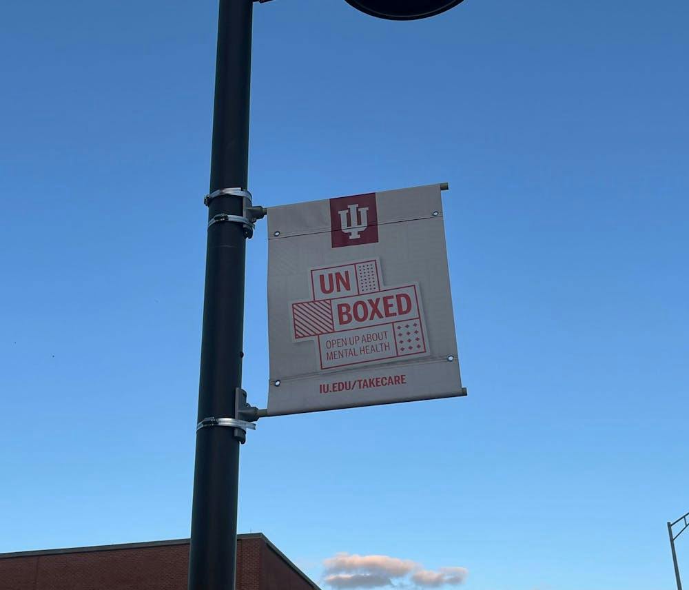 Photo of a lightpost on campus that has a sign for "Unboxed" with the link to iu.edu/takecare.