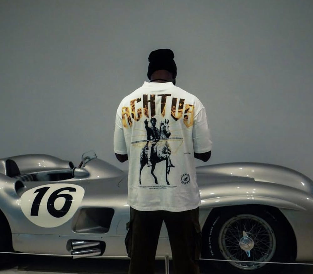 Purdue University student and Acktus founder Oluwatomi Oladunni wears a shirt from his brand’s collection during a photoshoot in front of a classic race car. (Photo Courtesy of Acktus)