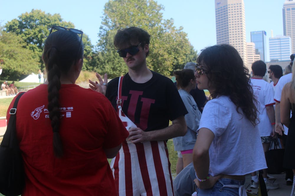 Students gather along the canal during the IU Indianapolis Regatta, with one participant showing school spirit in candy-striped overalls as the downtown skyline rises in the background.