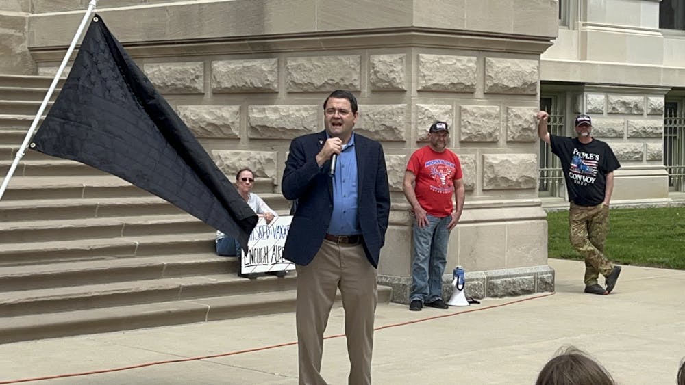 <p>Jon Schrock, field representative for the John Birch Society, speaks beside a radical &quot;Give no Quarter&quot; Flag</p>