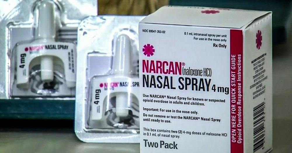 A two-pack box of Narcan nasal spray, containing two 4-milligram doses of naloxone, sits beside two individual nasal spray devices in their packaging. (Photo courtesy of CBS News)