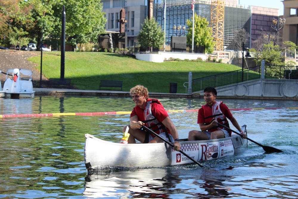 Two paddlers push their canoe forward during the IU Indianapolis Regatta, smiling as they race down the downtown canal on a sunny afternoon.