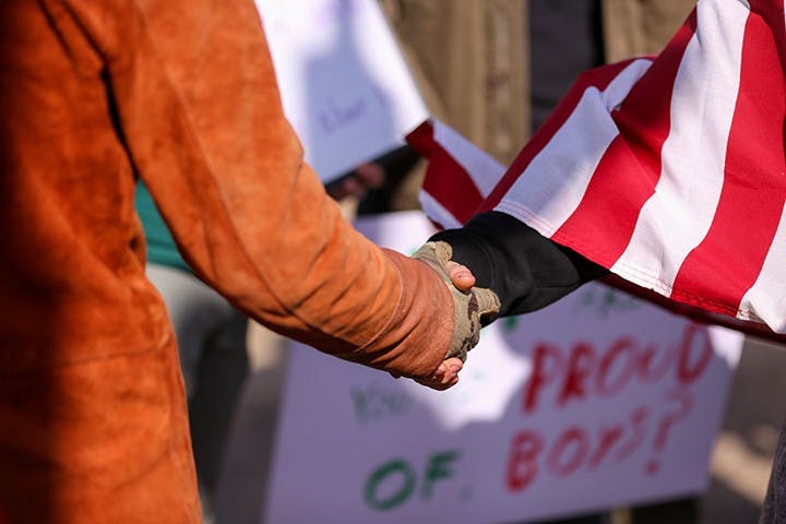 A member of the “Drive4America” caravan (right) shakes hands with a counter-protester (left) after the two groups met and voiced their frustrations.&nbsp;