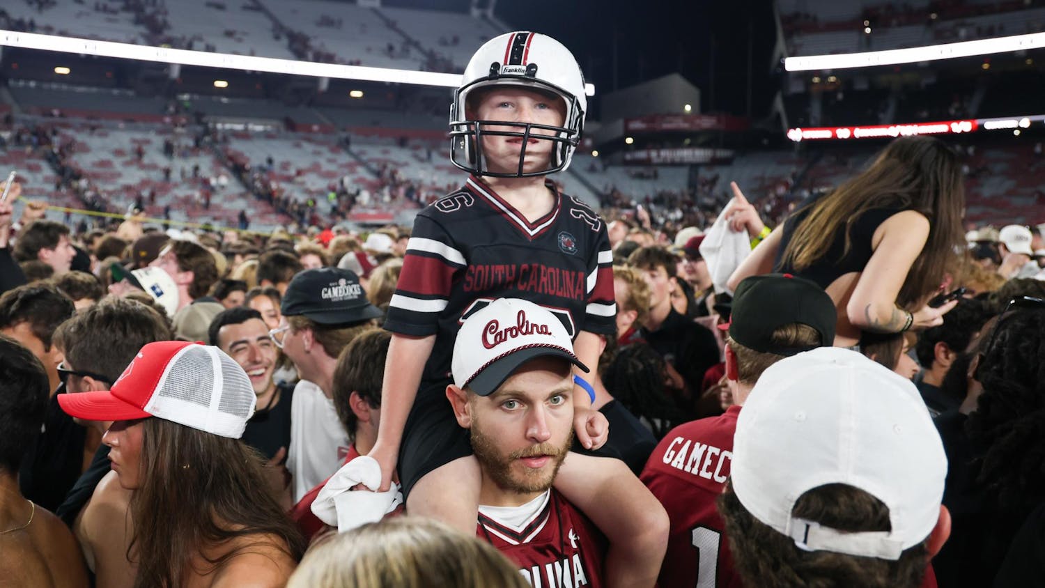 FILE – A young South Carolina fan sits on a man's shoulders in a crowd of people on the field at Williams-Brice Stadium on Nov. 2, 2024. South Carolina students and fans rushed the field after the team defeated then-No. 10 Texas A&M for the school's homecoming game.