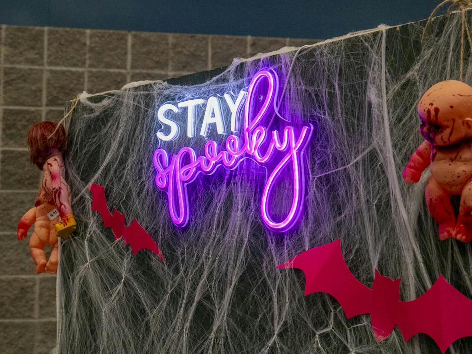 A photo backdrop with bats, bloodied baby dolls and a neon-sign reading "Stay Spooky" sits to the side of The Piercing Parlor booth at the South Carolina Horror Convention on Sept. 16, 2023. The piercing studio is based out of Irmo, South Carolina, and is ran and employed by women.