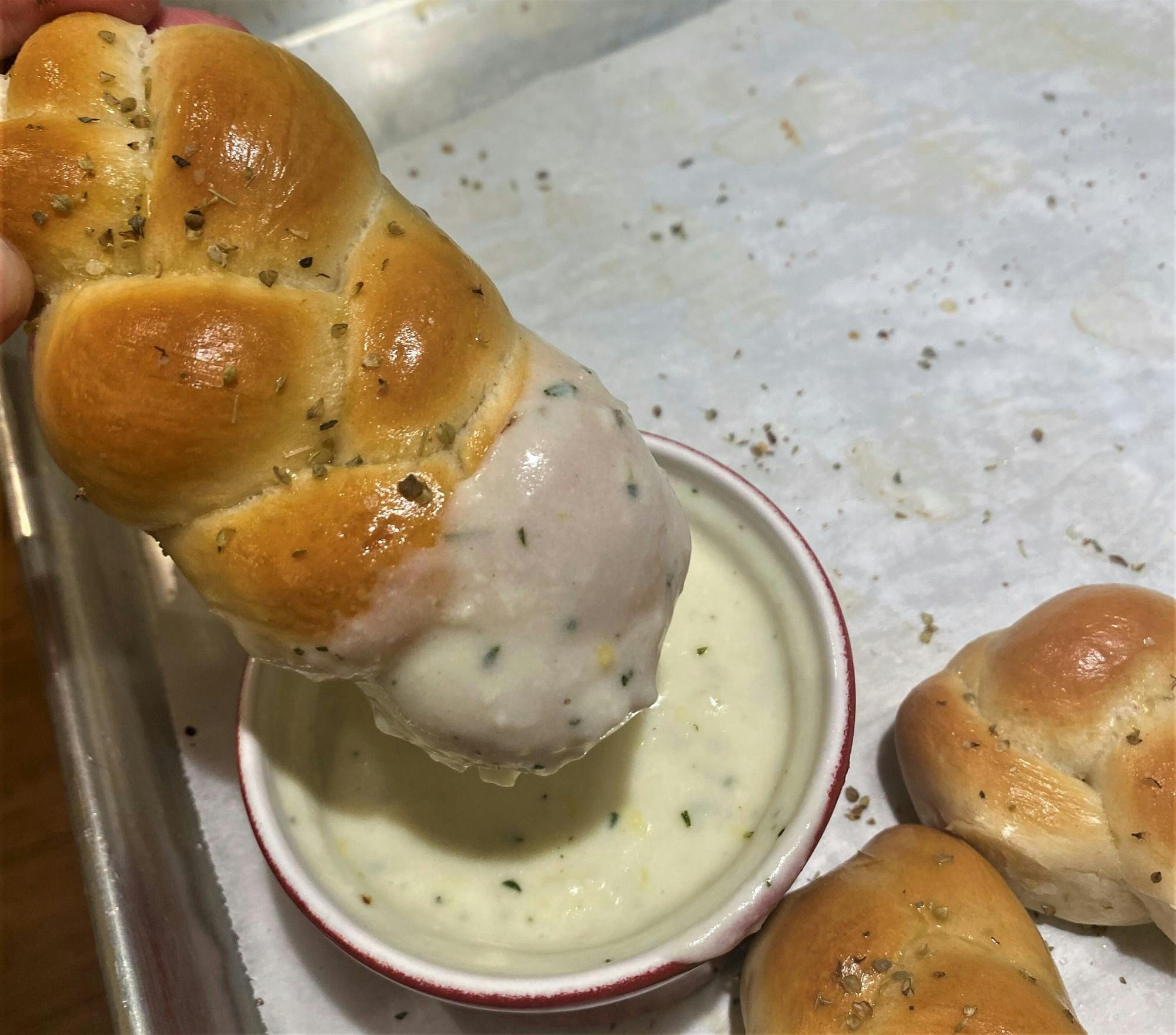 A picture of braided breadsticks dipped in a delectable cheese sauce.
