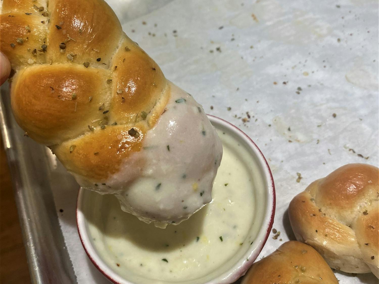 A picture of braided breadsticks dipped in a delectable cheese sauce.