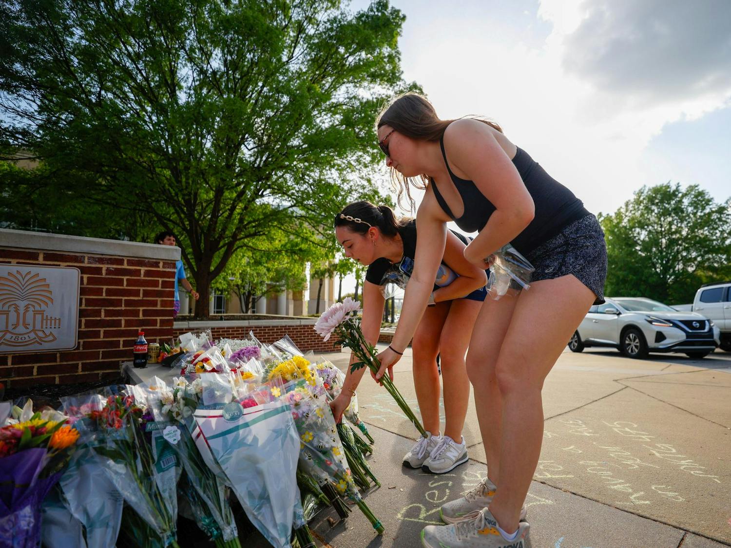 Two students place flowers at the memorial for Nathaniel "Nate" Baker outside Strom Thurmond Wellness and Fitness Center on April 3, 2025. Various student and faculty left flowers and other gifts in memory of Baker.