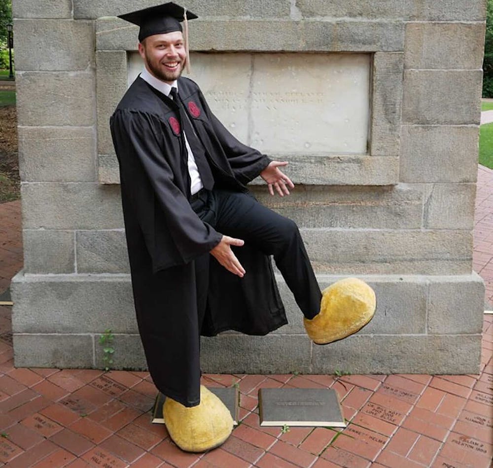 Matt Hammett wearing his graduation gown and the feet of the Cocky mascot. The student who is Cocky keeps their identity secret during their time at USC.