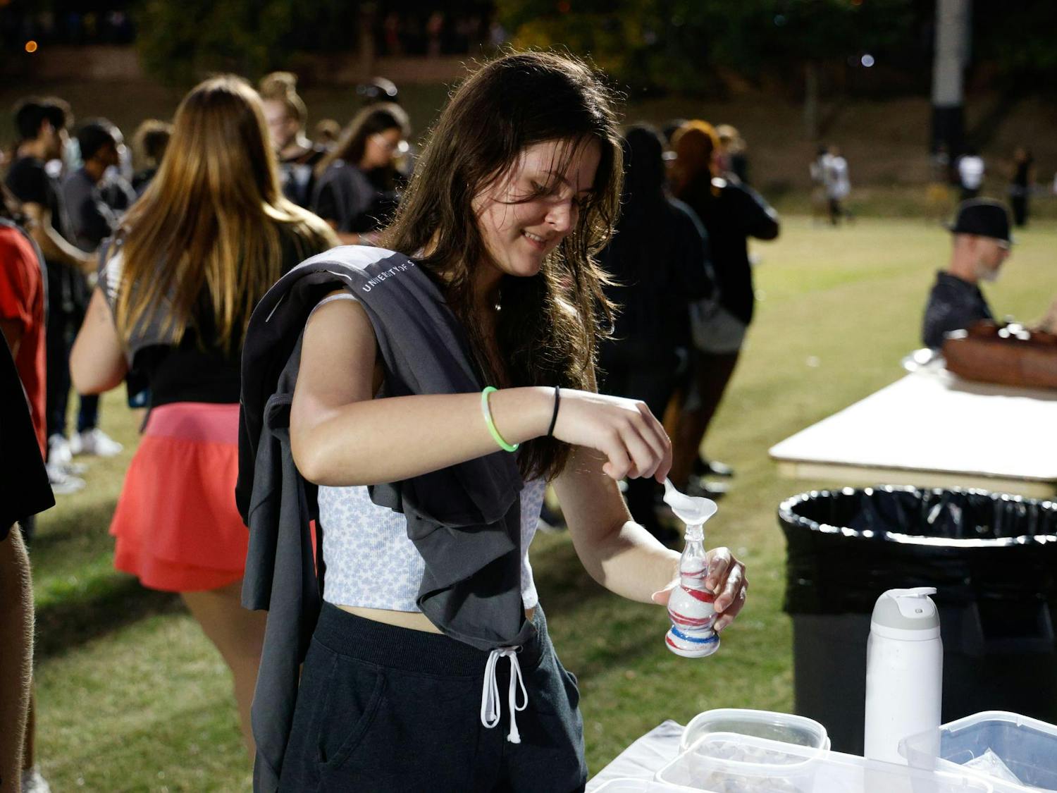 A student pours sand into a plastic jar at a sand art booth at Blatt Bonanza on Sept. 18, 2024, at Blatt Field. Students could choose from a variety of colors to create patterns in the containers.