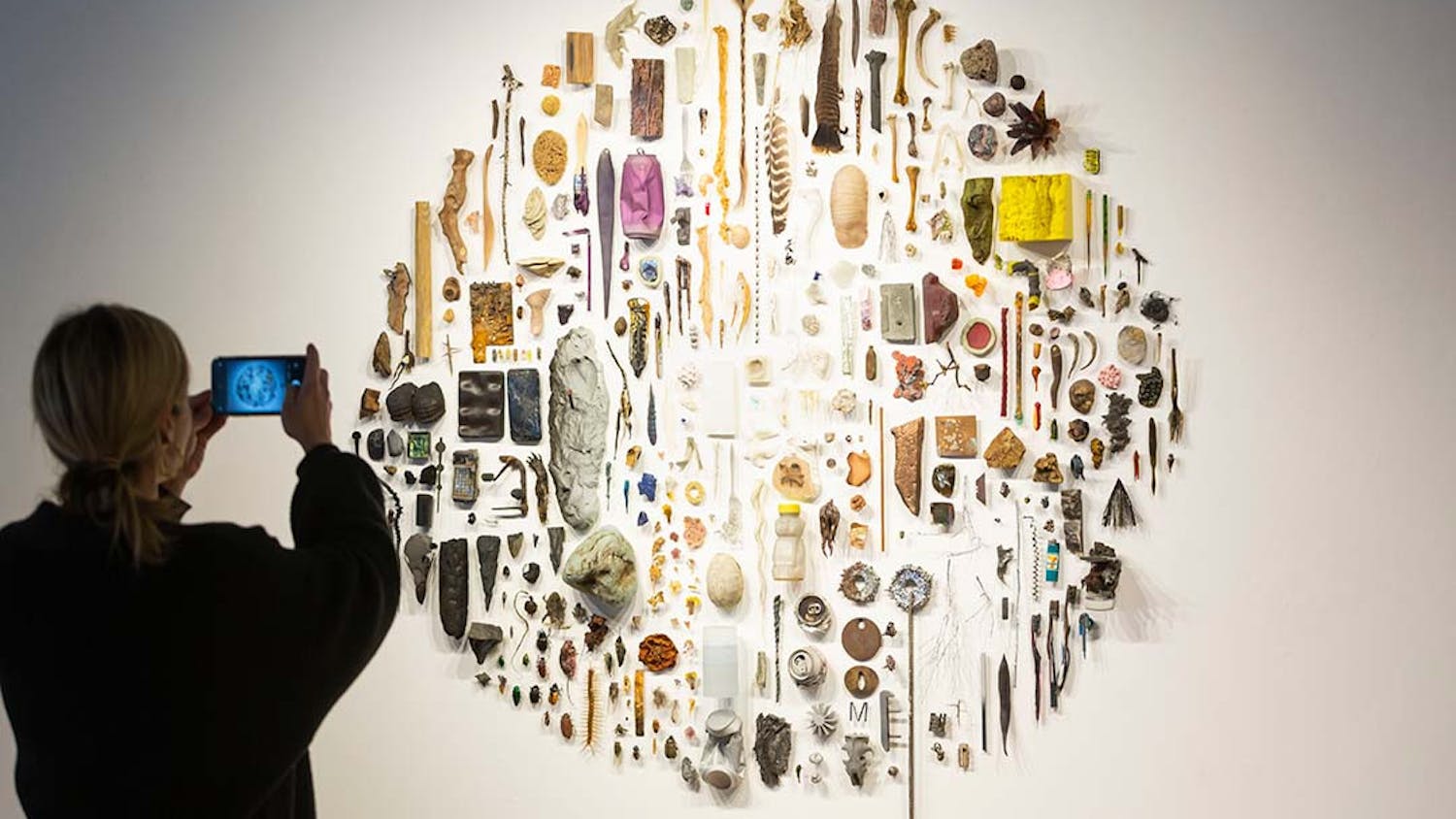 A visitor takes a photo of "Some Things" by Christopher Mahonski in the Voyage of Life exhibit featured in the McMaster Gallery. The sculpture is a collection of found and fabricated materials to explore the subject of ecological uncertainty.